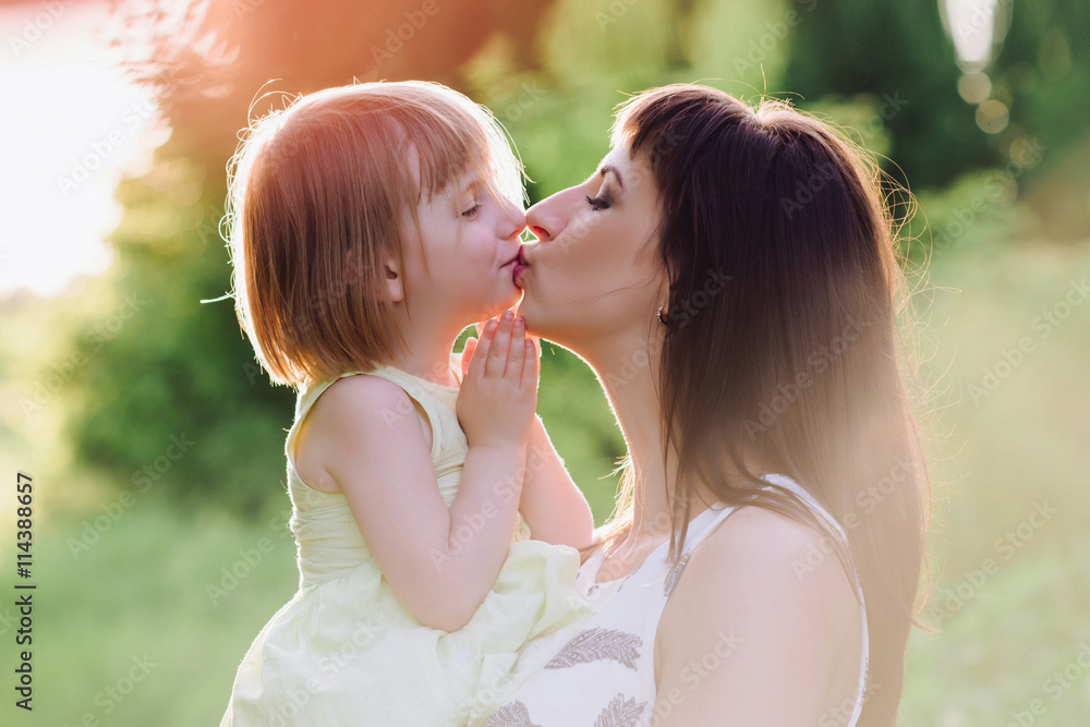 Mom kisses and hugs daughter on nature, family, motherhood, child Mom kisses and hugs daughter on nature, family, motherhood, child