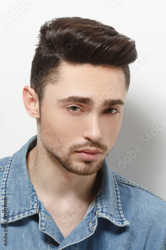 Portrait of young model man demonstrating his gorgeous and luxurious hair in studio. Handsome male in jeans shirt over shite background.