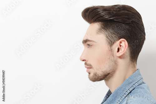 Profile of handsome young man injeans shirt posing over white background. Male with modern hairstyle in studio. Hairdressing concept.