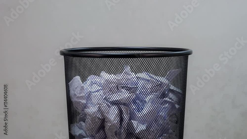 An empty office trash basket gets filled up with waste papers. Stop motion