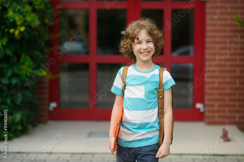 The little schoolboy stand on a schoolyard and joyfully smiles.