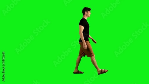 young man in full shot walking sideways over a green screen, looking back joyfully.