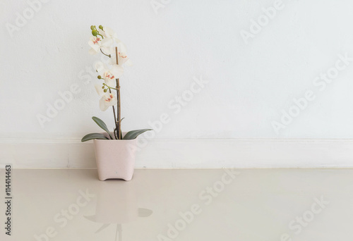 Fototapeta Naklejka Na Ścianę i Meble -  Closeup artificial plant with white flower on pink flower pot on blurred marble floor and white cement wall textured background , fake white orchid flower