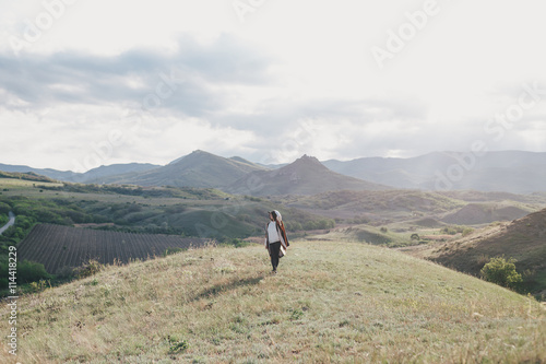 Young beautiful woman traveler wearing hat and poncho relaxing on the top of the hill with mountains and hills around