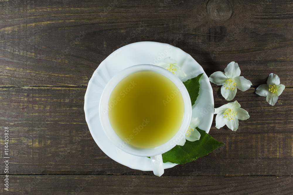 A cup of green jasmine tea standing in the center with white jasmine flowers A cup of green jasmine tea standing in the center with white jasmine flowers