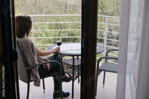 Young beautiful woman in a sweater sitting on a cozy terrace with a glass of red wine