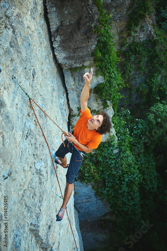 male rock climber. rock climber climbs on a rocky wall. man hanging on a rope and shows his hand up