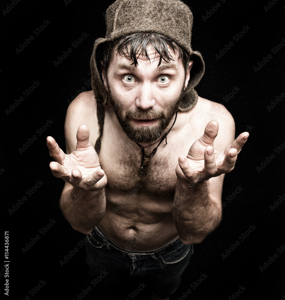 Dark portrait of scary evil sinister bearded man with smirk, makes various hand's signs and expresses different emotions. strange Russian man with a naked torso and a woolen hat