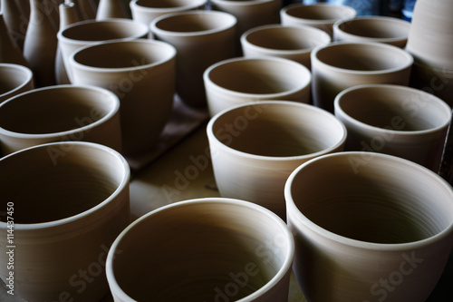 Many rustic handmade terracotta clay pots ready to be fired. Shallow depth of field. Selective focus.