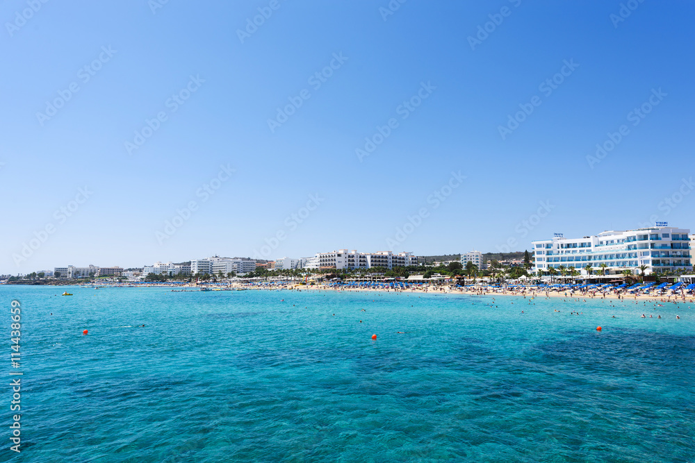 Photo of sea and fig tree bay beach in protaras, cyprus island with swimming people and hotels.