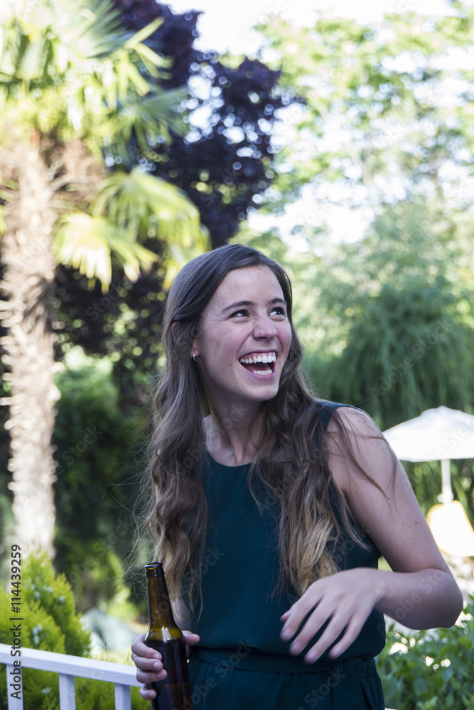 Woman laughing, holding a bottle of beer during a summer dinner in a garden Woman laughing, holding a bottle of beer during a summer dinner in a garden
