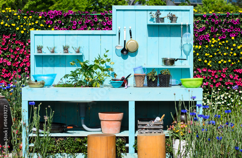 Obraz na plátně Blue wooden outdoor kitchen and kitchen wares hanging on with flowers garden background