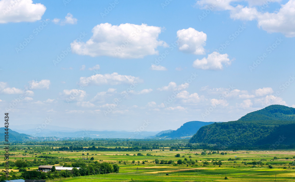 Country landscape in mountain valley with farmland on blue sky