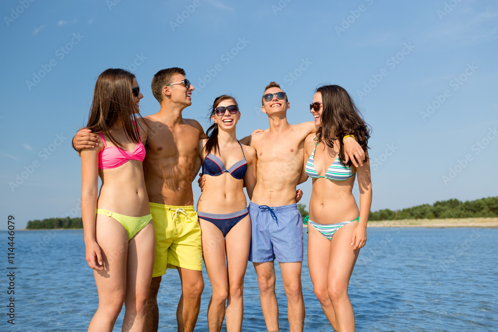smiling friends in sunglasses on summer beach