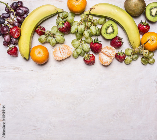 Delicious assortment of fresh fruit laid out in a border on a white rustic background top view Superfoods and health or detox diet food concept