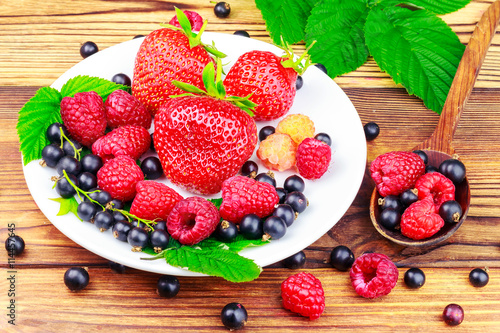 Photos Mix of fresh, ripe berries in plate and spoon on wooden background