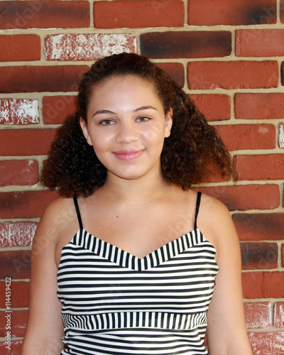 Pretty, Ethnic, Teenage Girl Smiling Against Brick Wall