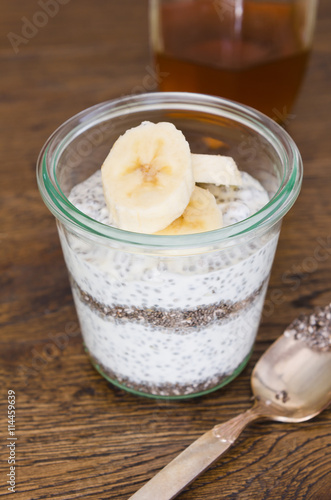 Organic yoghurt, sliced banana, chia seeds, served in a clean glass glass cup.