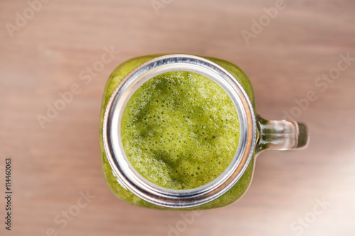 A top view of a green smoothie in a mason jar on wooden background