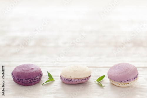 French purple macaroons horizontal line copyspace. Sweet macaroons put in hirizontal line in downside of pictire on white wooden background. Macaroons line decoratrd with mint photo