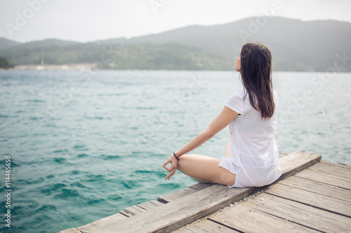 Yoga and meditation concept.Woman meditating in sitting yoga position on pier.Woman alone practicing mindfulness meditation to clear her mind.Zen meditation peace concept