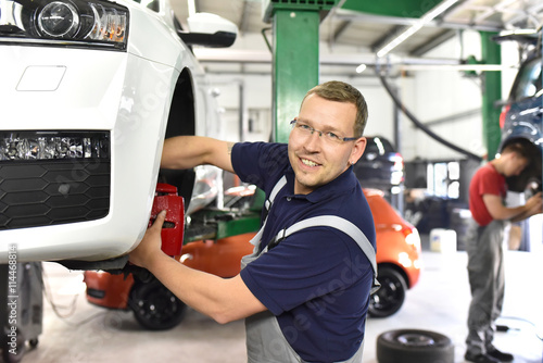 fröhlicher automechaniker repariert Bremsen am Fahrzeug in einer Werkstatt // car mechanic repairs brakes of a car in a garage