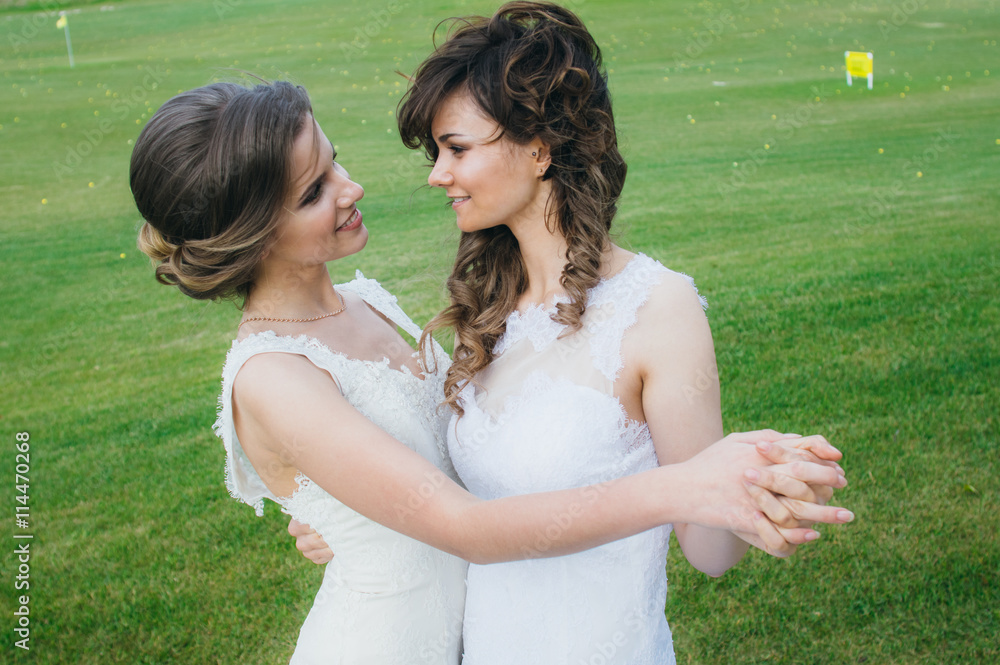 Two beautiful brides dancing  on the green field of the golf club