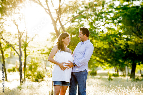 young happy couple in love together on park landscape sunset with woman pregnant belly