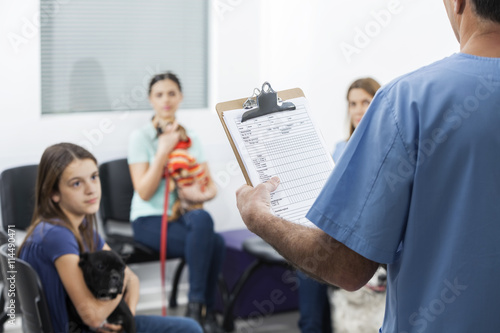 Nurse Holding Form While Owners With Pets Waiting In Hospital