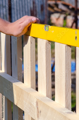 Man building a wooden fence and checking with spirit level. Clos
