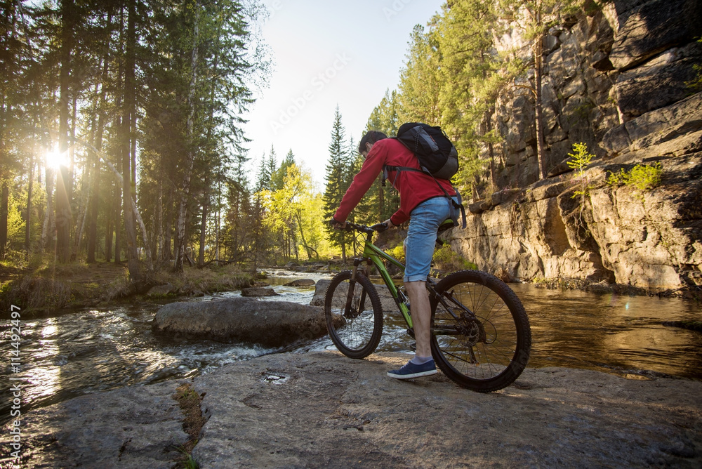 Cyclist with a backpack traveling on a mountain river at sunset Cyclist with a backpack traveling on a mountain river at sunset