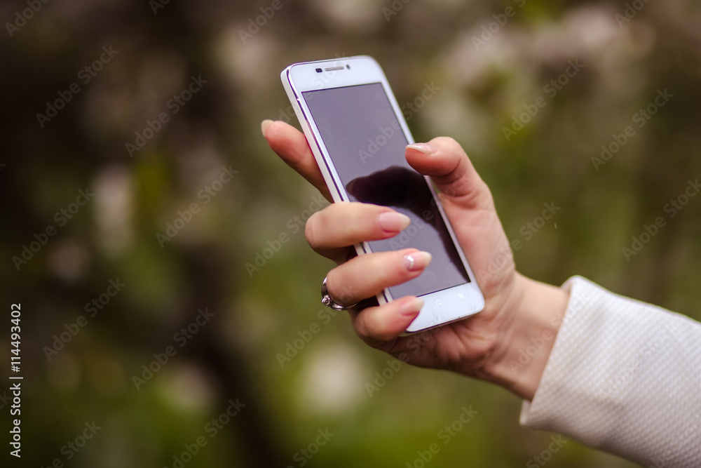 woman holds a smartphone telephone over blossoming spring tree background, soft focus, close up