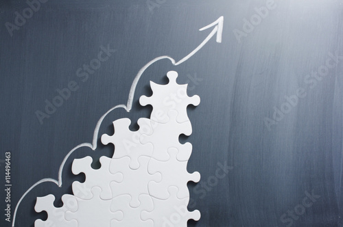 Steps shaped jigsaw puzzle and up arrow on blackboard. Concept image of making growth strategy. 
 photo