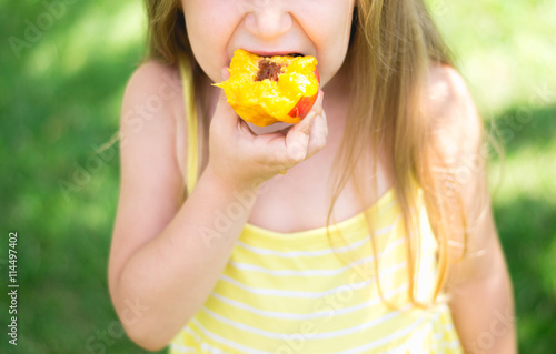 Little girl is eating peach, close-up
