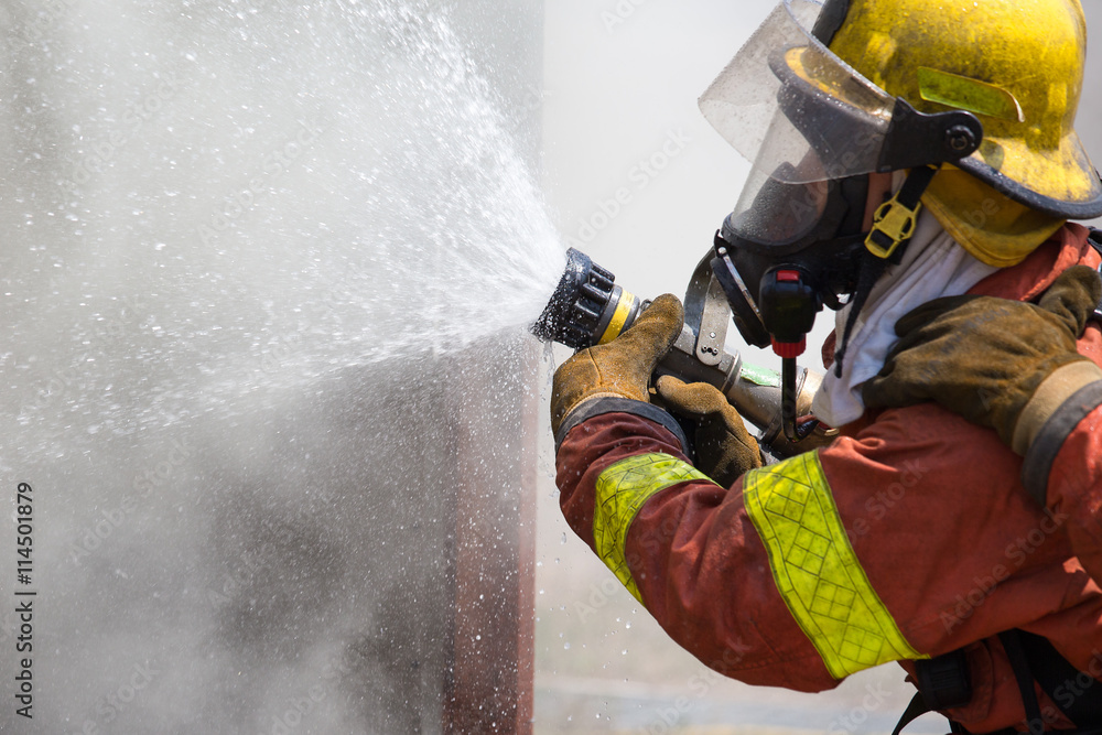 Fototapeta premium fireman in fire fighting suit spraying water to fire surround wi