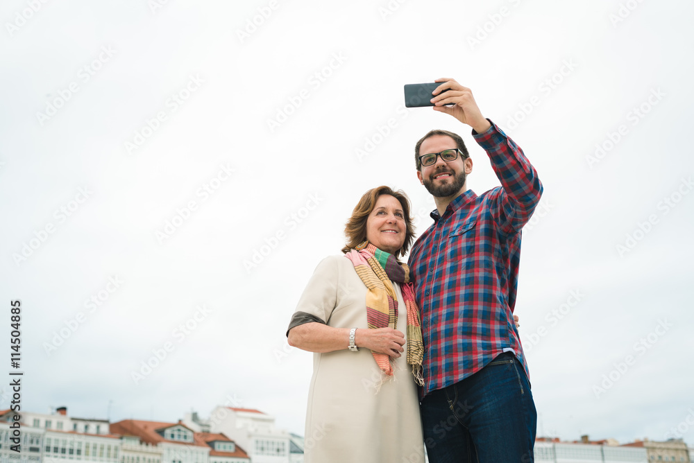 Smiling Mother and son using smartphone for taking a selfie photograph. Urban maritime vacations on summer.