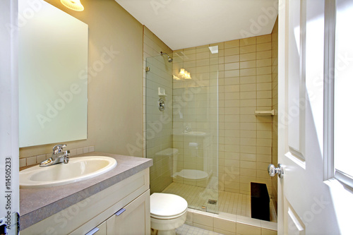 Nice creamy bathroom interior with glass shower and white cabinet with mirror.