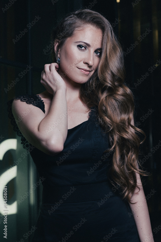 Beautiful girl standing near shopwindow on the night city street. Fashion style portrait of young pretty beautiful woman with long dark curly hair Beautiful girl standing near shopwindow on the night city street. Fashion style portrait of young pretty beautiful woman with long dark curly hair