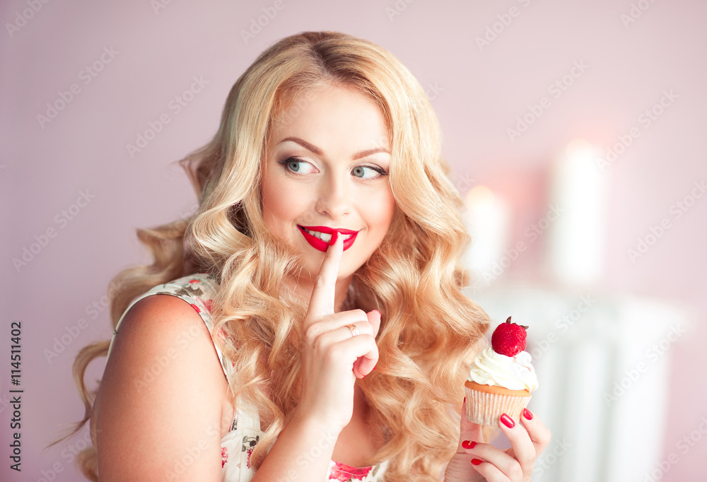 Smiling woman holding cupcake with strawberry in room. Looking away. Smiling woman holding cupcake with strawberry in room. Looking away.