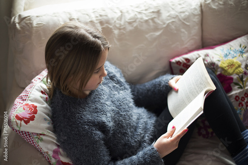 Girl reading book while sitting on sofa