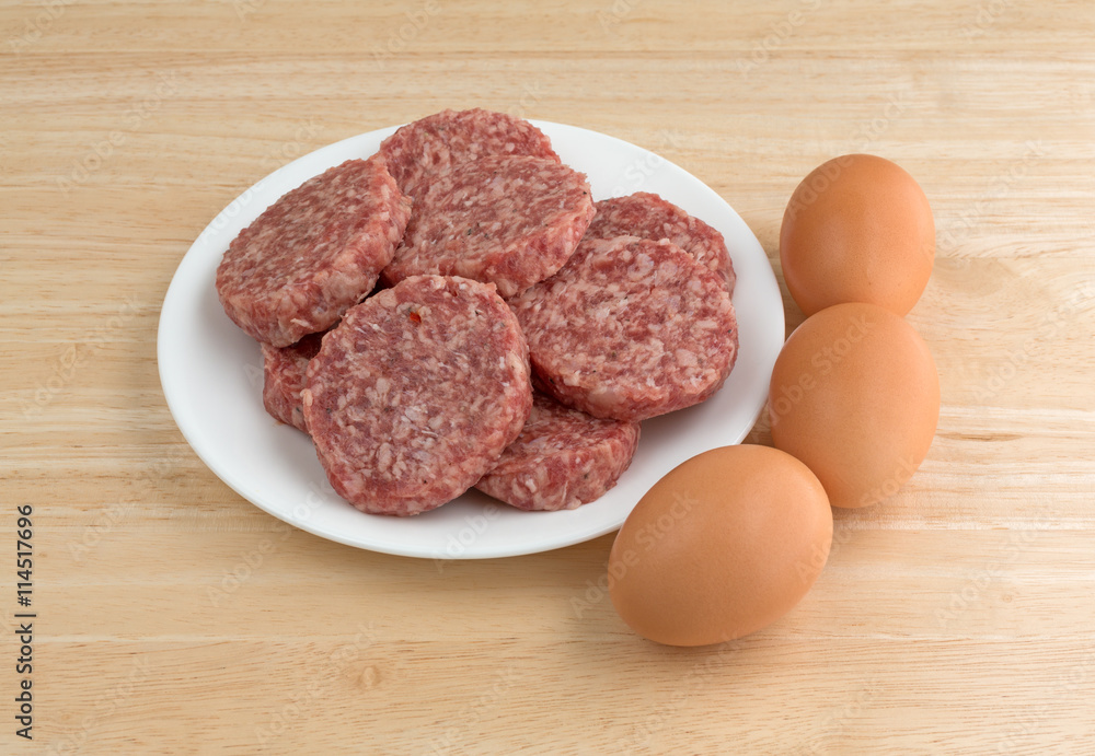 Sausage patties on a white plate with eggs to the side on a wood counter top. Sausage patties on a white plate with eggs to the side on a wood counter top.