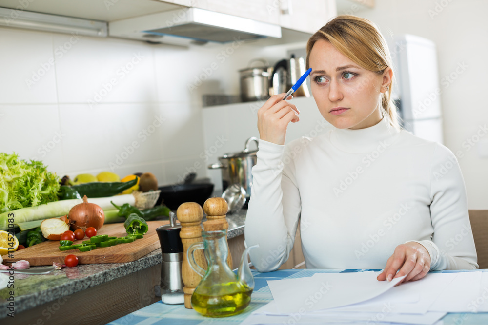 Upset woman calculating budget in kitchen