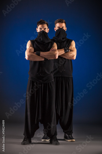 Two male dancers posing in ninja costumes against blue backgroun