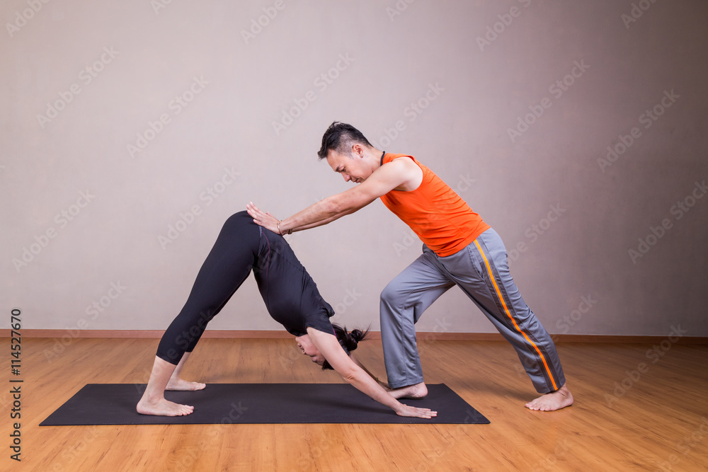 Yoga instructor guiding student perform downward facing dog pose