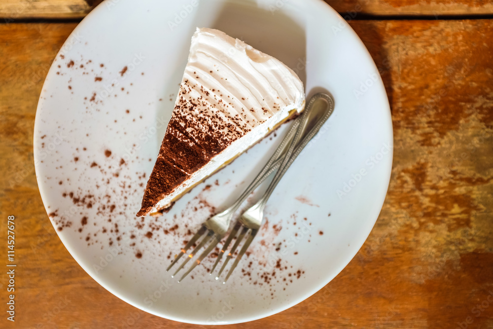 White cake with chocolate in white plate on wooden table in cafe White cake with chocolate in white plate on wooden table in cafe