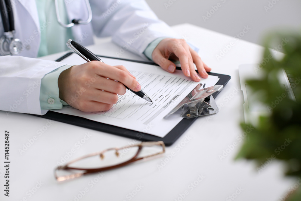 Close-up of a female doctor filling out application form , sitting at the table in the hospital Close-up of a female doctor filling out application form , sitting at the table in the hospital