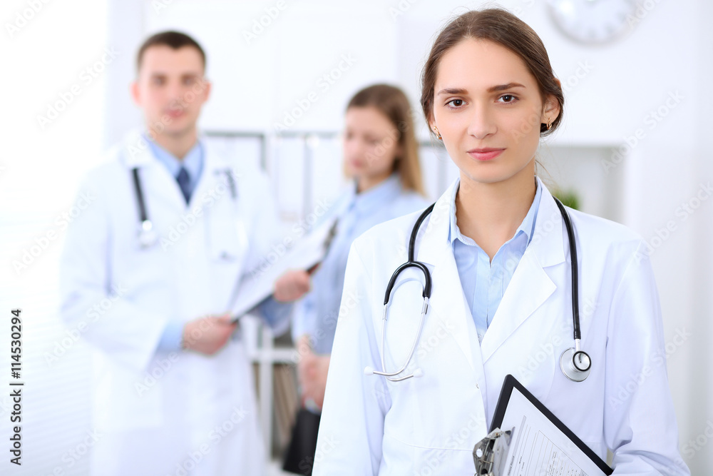 Young beautiful female doctor smiling on the background with patient and his doctor in hospital. High level and quality medical service concept. Young beautiful female doctor smiling on the background with patient and his doctor in hospital. High level and quality medical service concept.