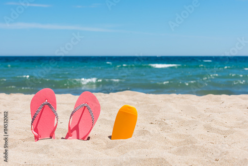 Sunscreen bottle and pink flip flops on the beach