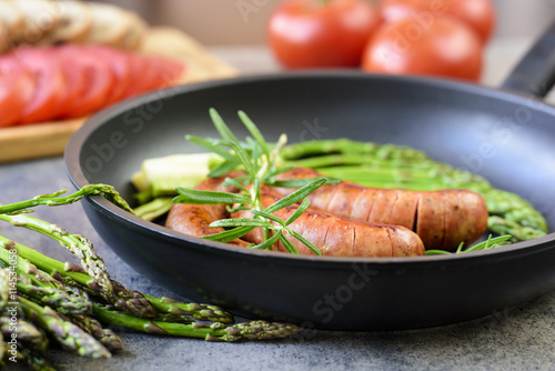 sausages with asparagus, tomatoes and rosemary on a pan