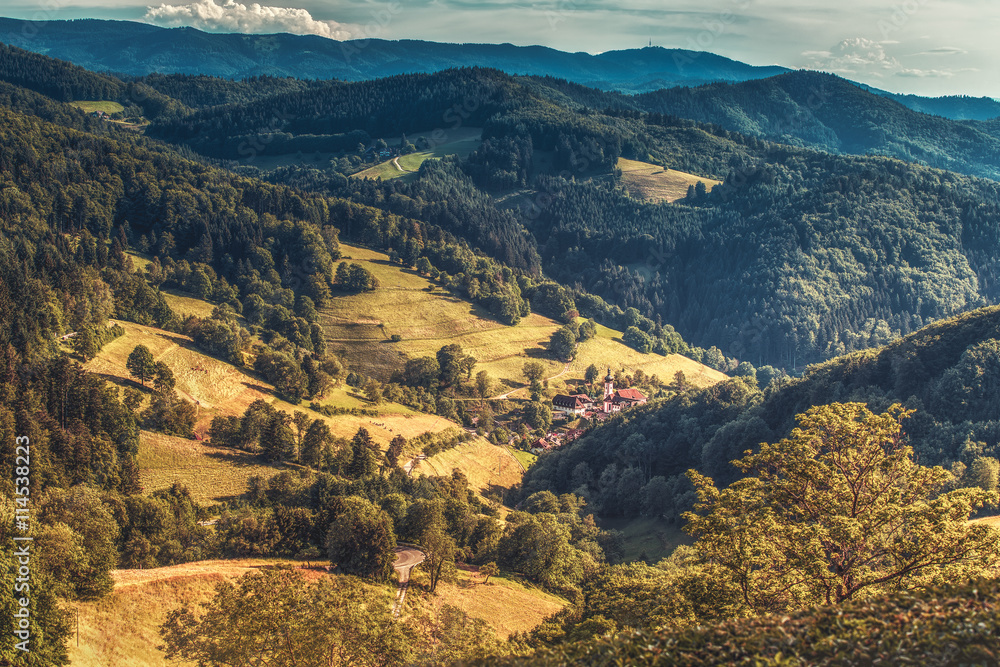Scenic countryside landscape: summer mountain valley with forests, fields and old church in Germany, Black Forest